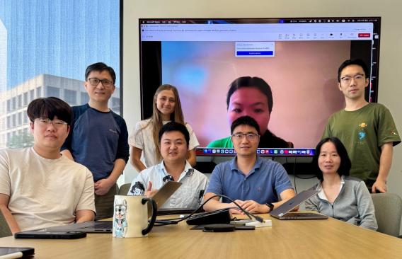 A group of people posed behind a table, in front of a large screen.