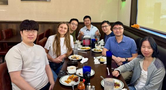 A group of people posed around a restaurant table with food and drink.
