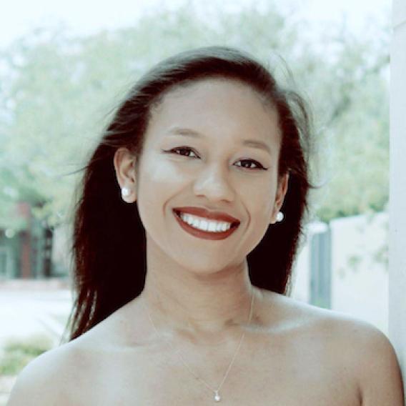 Woman with long dark hair and a huge smile, pearl earrings and a pendant necklace.