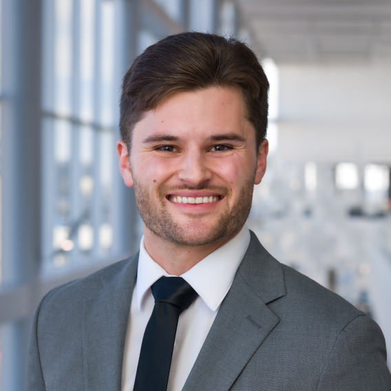 Smiling man with dark hair and facial hair, wearing a suit and tie.