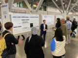 a group of attendees listen to Julian Merville explain poster presentation