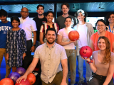 Large group of people pose for camera in front of bowling alley lanes